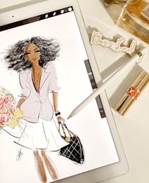 A digital illustration of a stylish woman with curly hair on a tablet screen, holding a bouquet of flowers and a quilted handbag. Next to the tablet, there is a stylus, lipstick, a bottle of perfume, and a decorative 'Boss Lady' sign.
