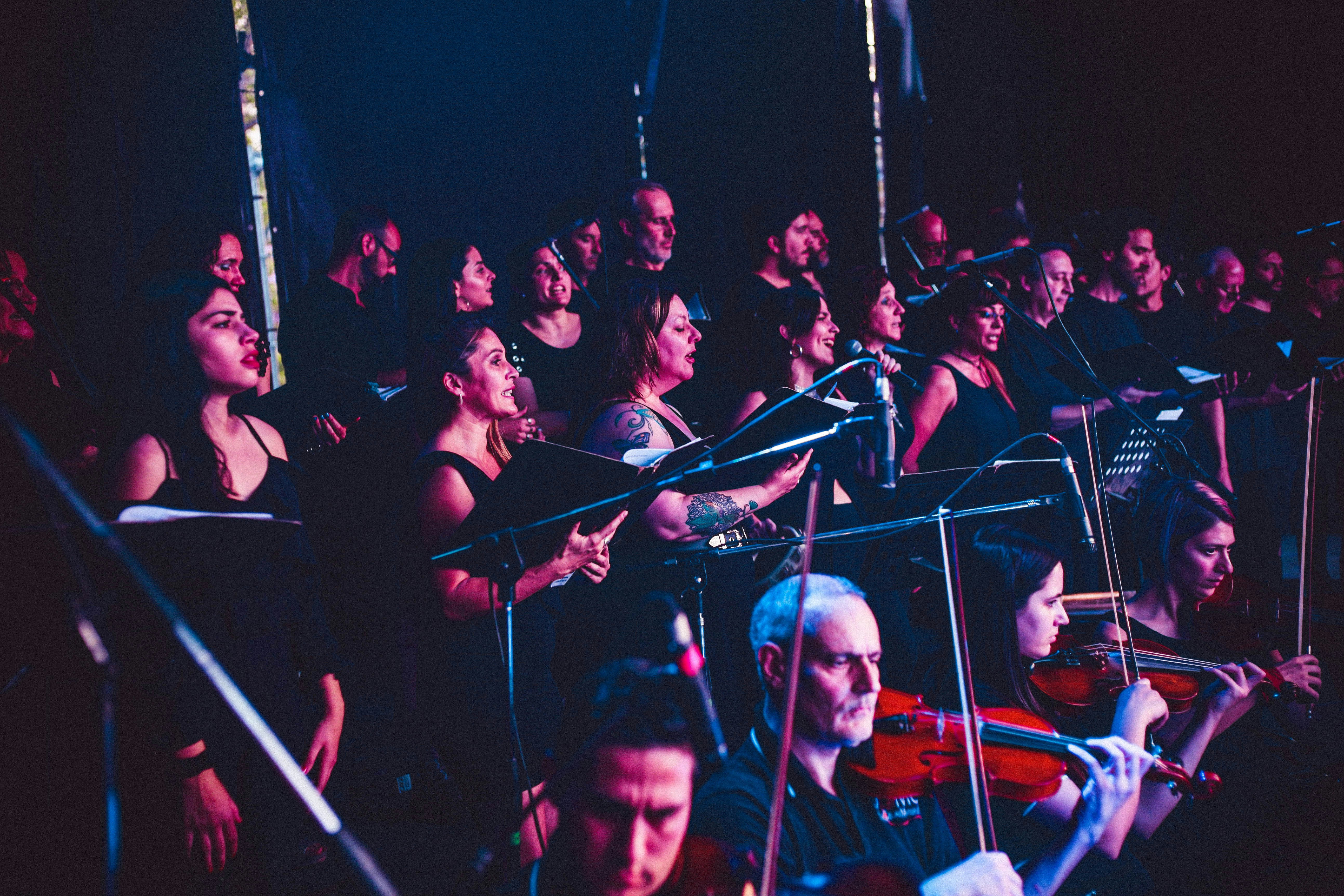 Large diverse musical ensemble performing on stage with colorful stage lighting
