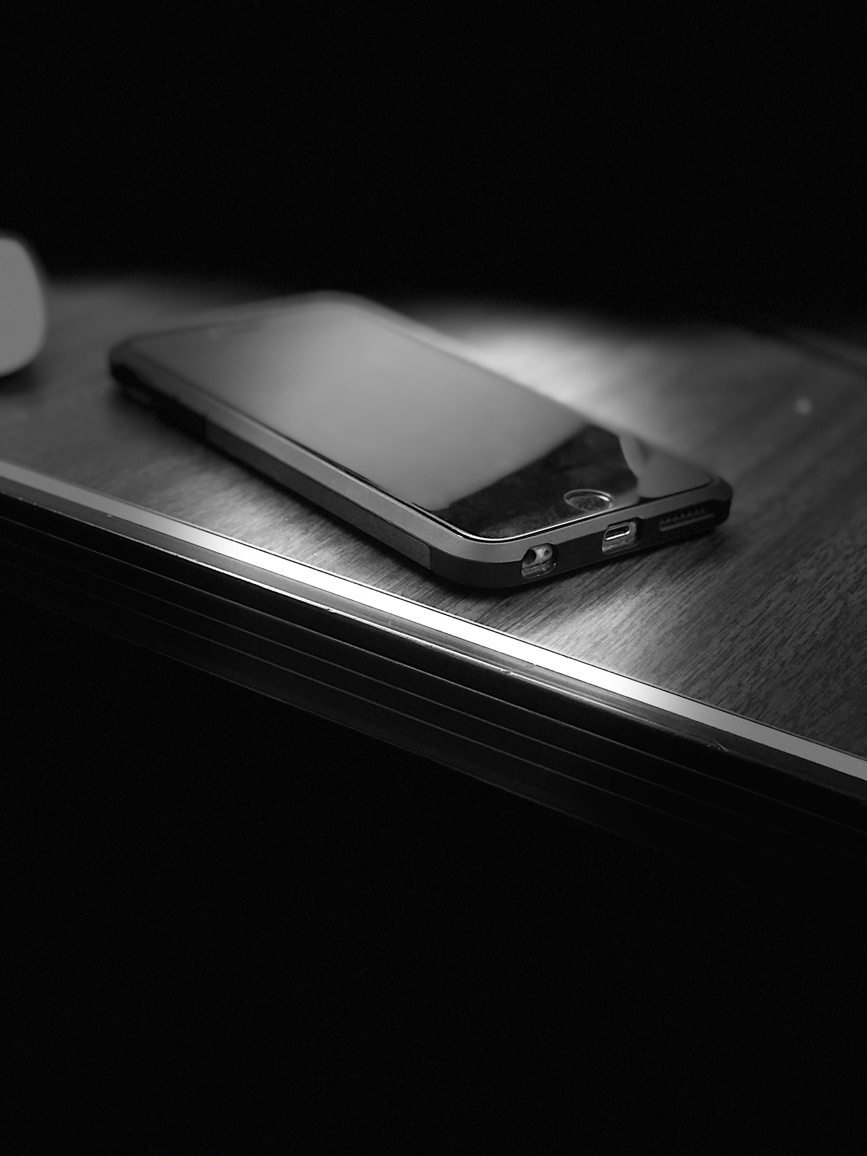 Smartphone showing shopping app with product listings on a dark desk surface, dramatic side lighting, deep shadows