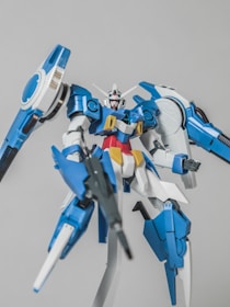 A highly detailed model of a futuristic blue and white robot with various angular components and weaponry. The robot has a sleek design with red, yellow, and gray accents, featuring large appendages that suggest advanced technology and flight capability.