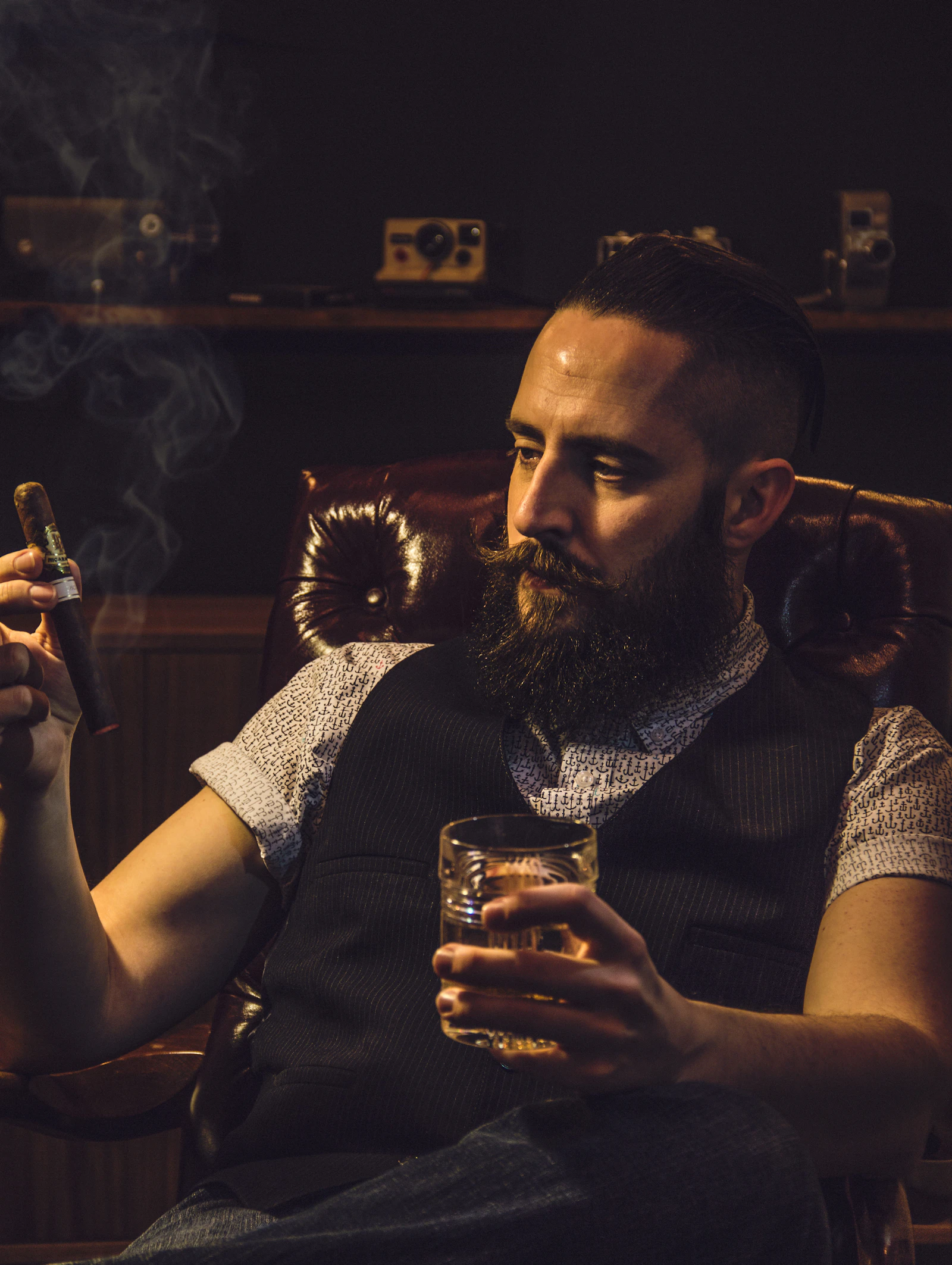 Executive holding a cigar and scotch glass in low warm light