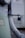 An outdoor electrical meter box attached to a wall, with a thick gray conduit pipe leading downwards. A rusty padlock is affixed to a latch, providing a sense of security. There are warning labels and some exposed wires visible.