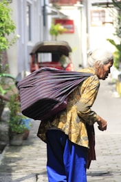 A caregiver helping an elderly person with a shopping bag outdoors.