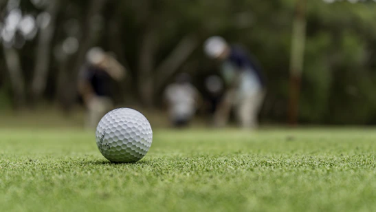 Close-up of a football resting on green grass with blurred players in the background