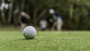 A close-up of a golf ball mid-air during a fundraising contest, with cheering participants in the background.