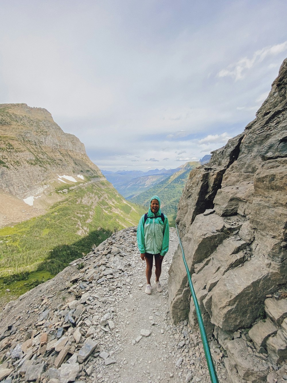 woman in green jacket and blue denim jeans standing on rocky mountain during daytime