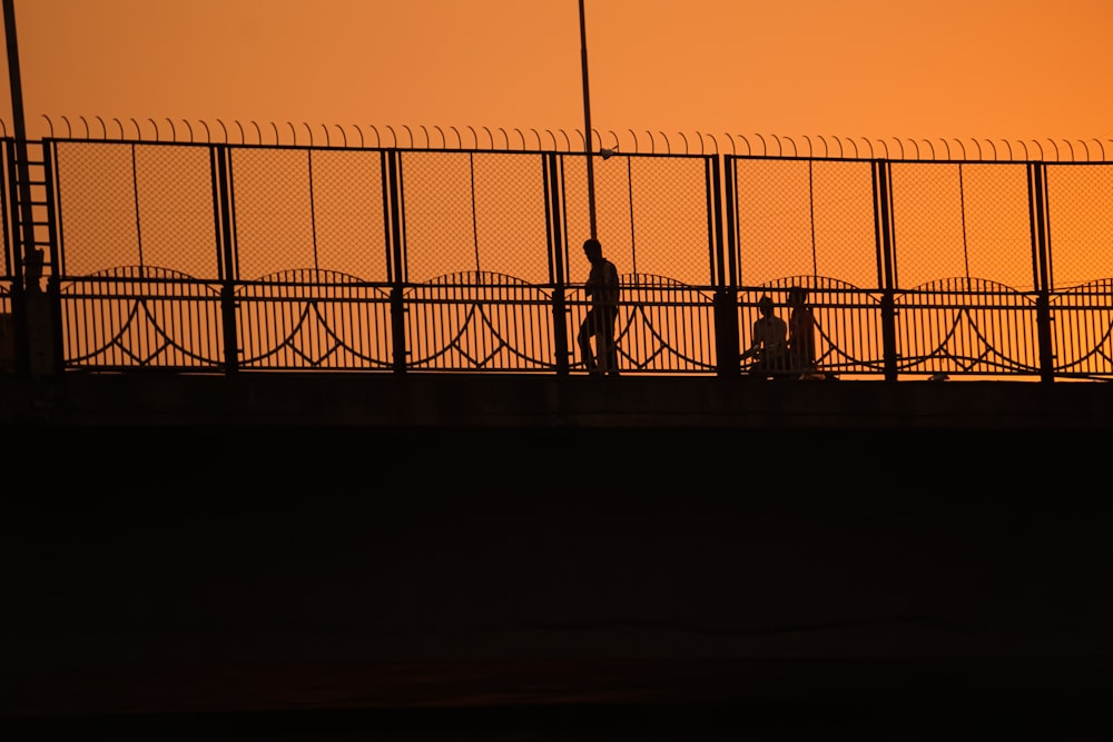 silhouette of 2 person standing near fence during sunset