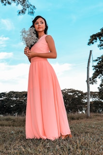 A gentle woman in a flowing peach dress holding a bouquet of lavender flowers in a sunlit garden.