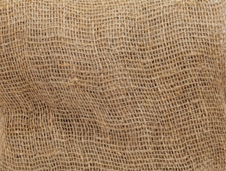 A close-up view of a brown burlap sack, highlighting its coarse and textured weave. The natural fibers create a rough surface pattern, characteristic of the rustic and utilitarian material.