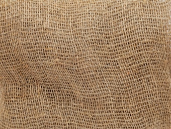 A close-up view of a brown burlap sack, highlighting its coarse and textured weave. The natural fibers create a rough surface pattern, characteristic of the rustic and utilitarian material.