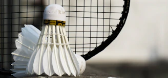 Close-up of a sleek badminton racket resting on a wooden floor with shuttlecocks nearby.