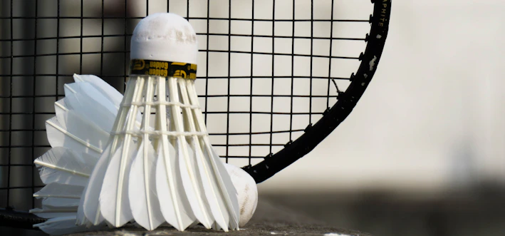 Close-up of a sleek badminton racket resting on a wooden floor with shuttlecocks nearby.