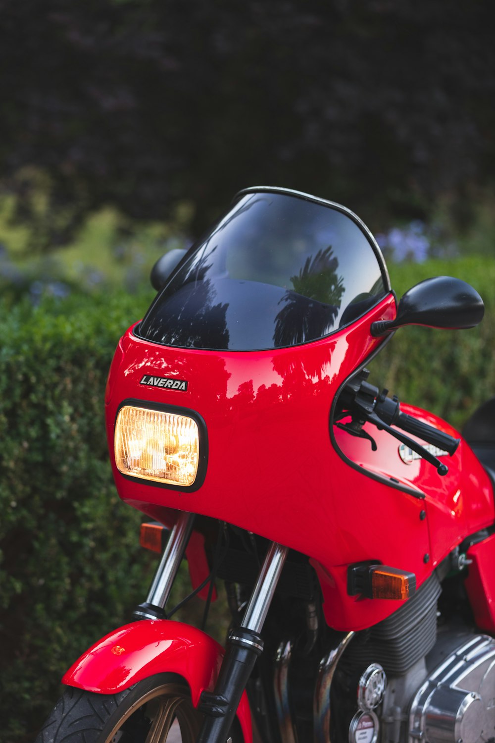 a red motorcycle parked next to a bush