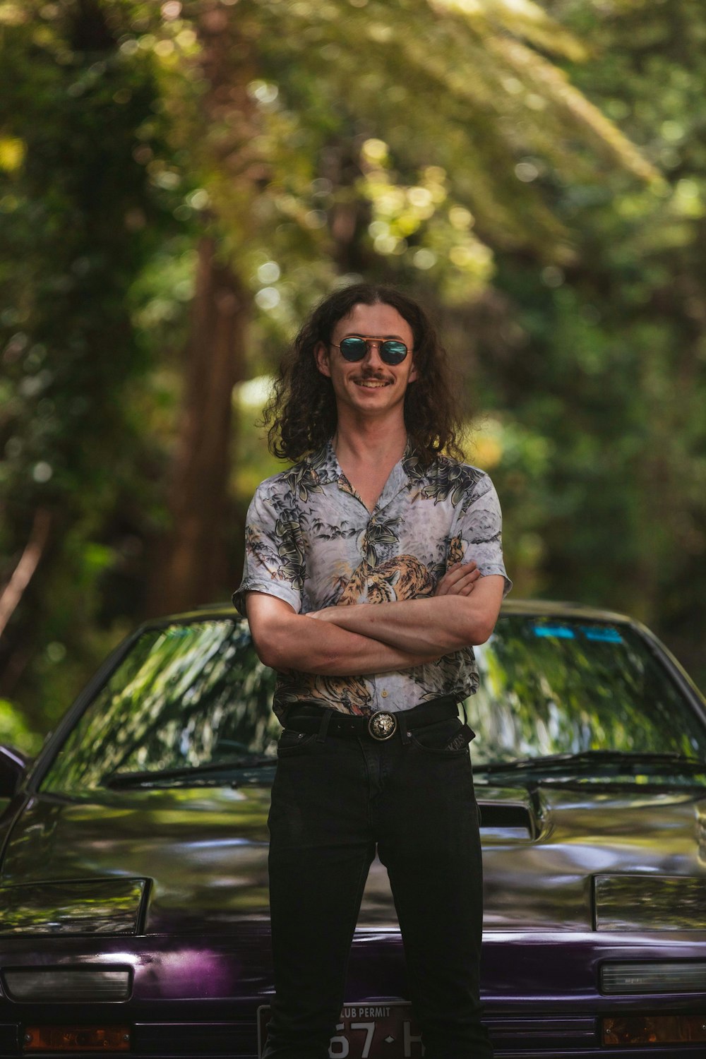 woman in blue and white floral shirt and black pants standing beside black car during daytime