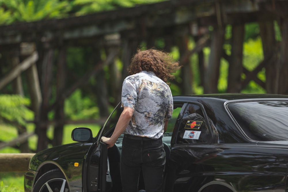 woman in white shirt and black pants standing beside black car during daytime