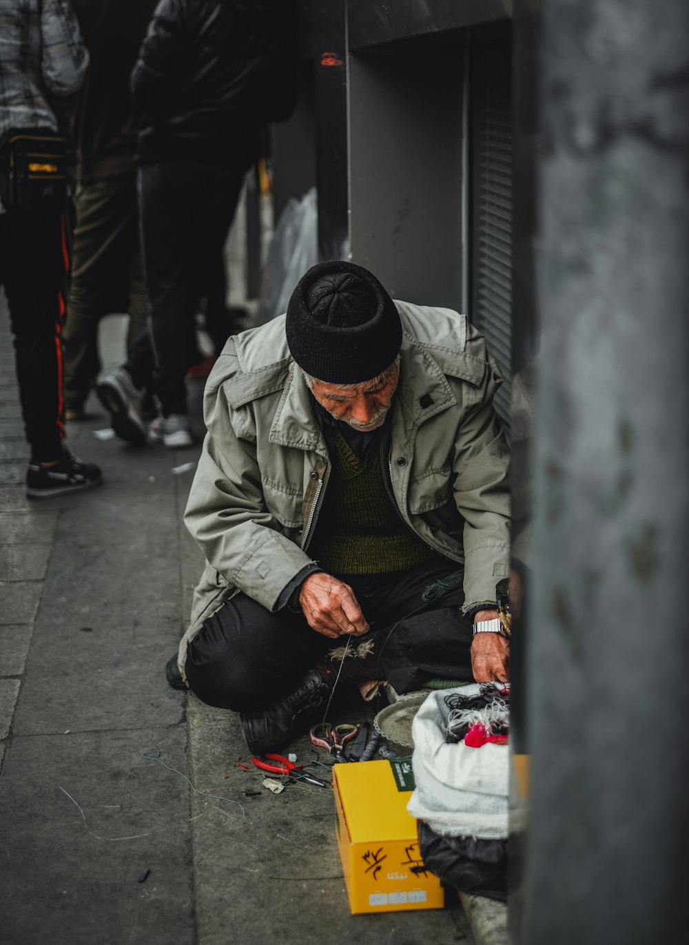 man in gray jacket and black knit cap sitting on sidewalk during daytime