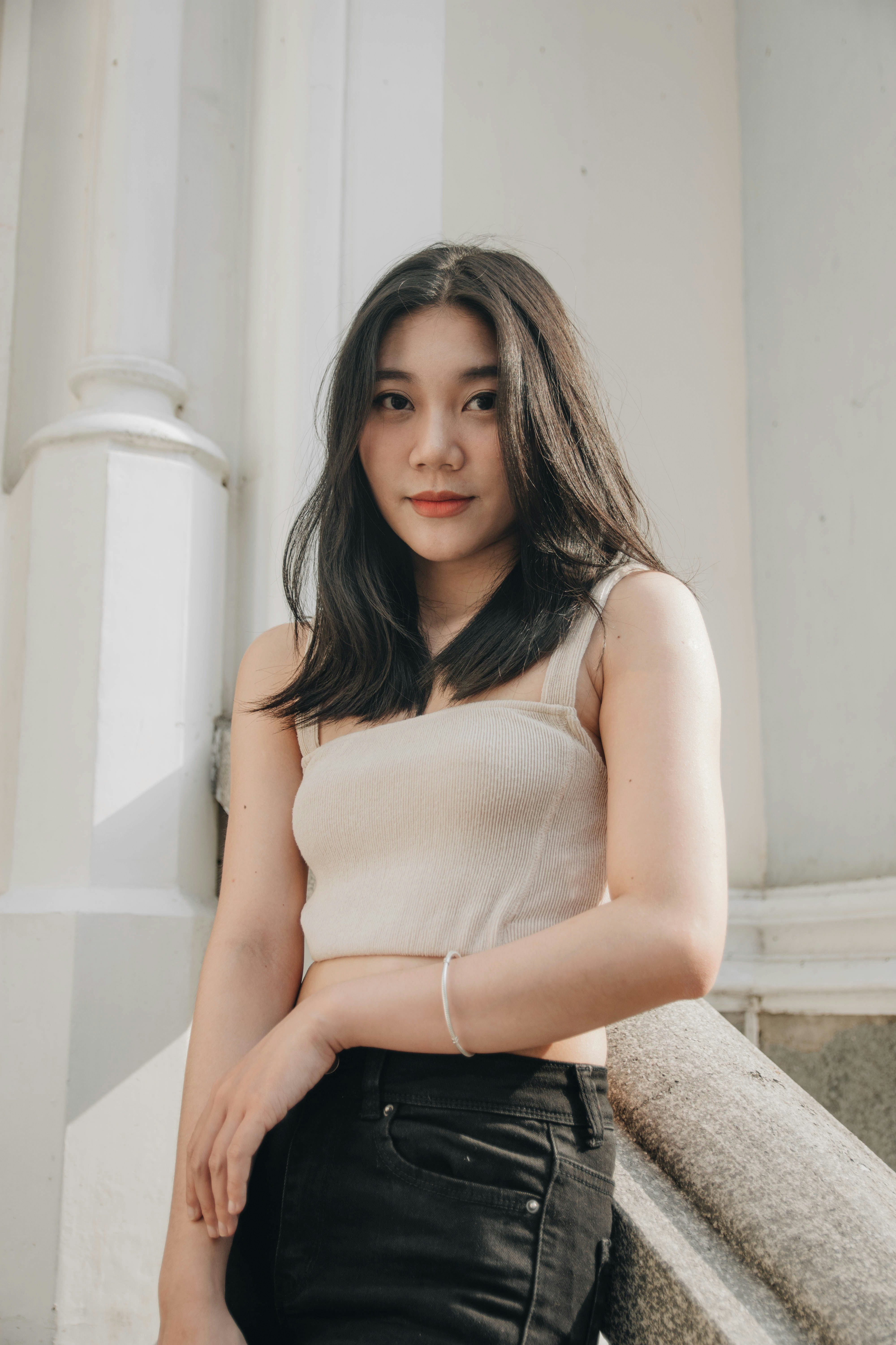 woman in white tank top and black denim bottoms sitting on white concrete bench