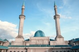 A large mosque with two tall minarets and a central blue dome under a clear blue sky.