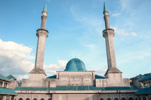A large mosque with two tall minarets and a central blue dome under a clear blue sky.