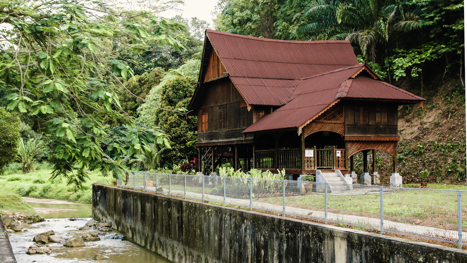 Rumah kampung kayu tradisional Malaysia di tepi sungai dikelilingi hutan hijau