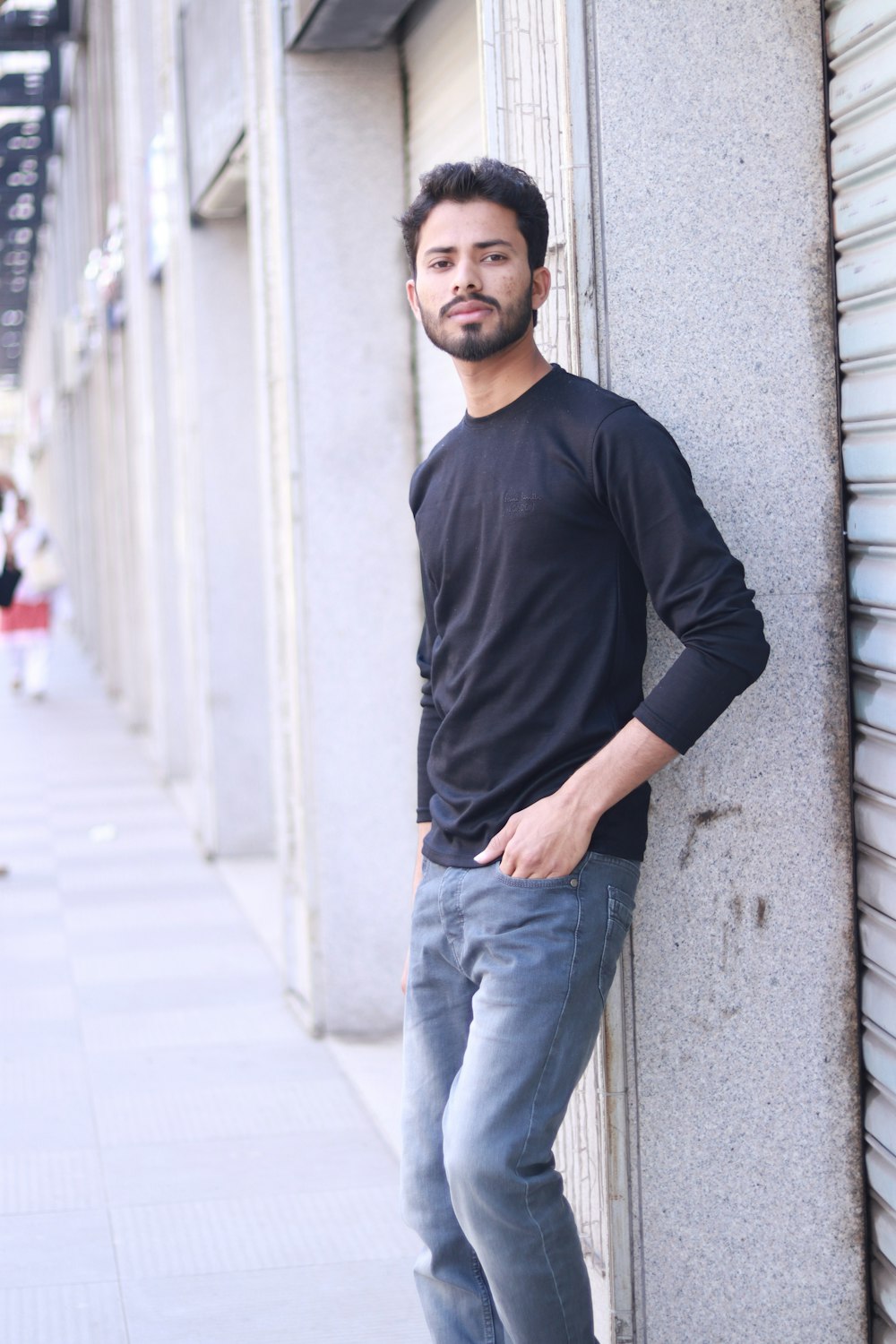 man in black long sleeve shirt and blue denim jeans leaning on wall