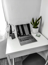 A sleek, minimalist workspace with a laptop and green plant on a white desk.