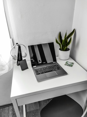 A minimalist workspace featuring a tablet, headphones, and a small potted plant.