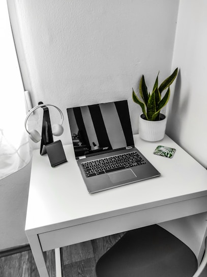 A serene workspace with soft natural light, a laptop, and headphones resting beside a small potted plant.