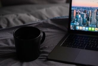 A coffee cup steaming beside an open laptop displaying a draft of a novel, set against a backdrop of city skyline.