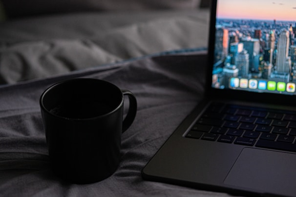 A coffee cup steaming beside an open laptop displaying a draft of a novel, set against a backdrop of city skyline.