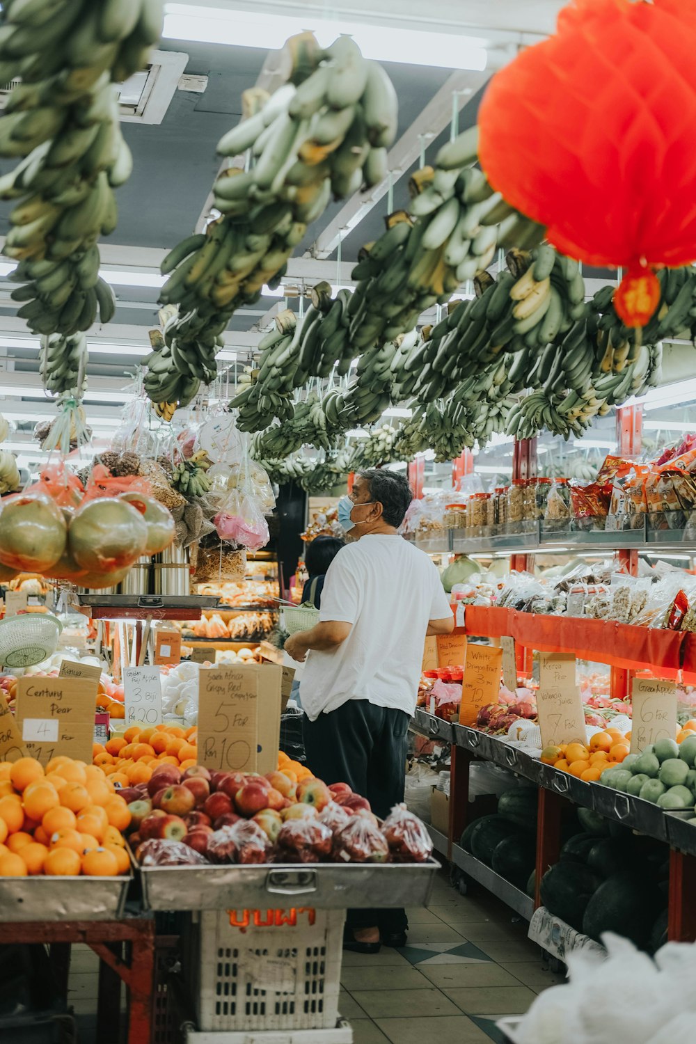 man in white t-shirt standing in front of fruit stand