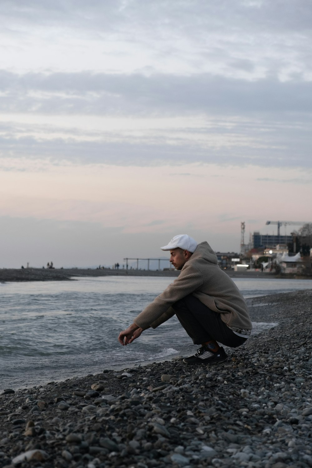 man in gray hoodie and black pants sitting on rocky shore during daytime