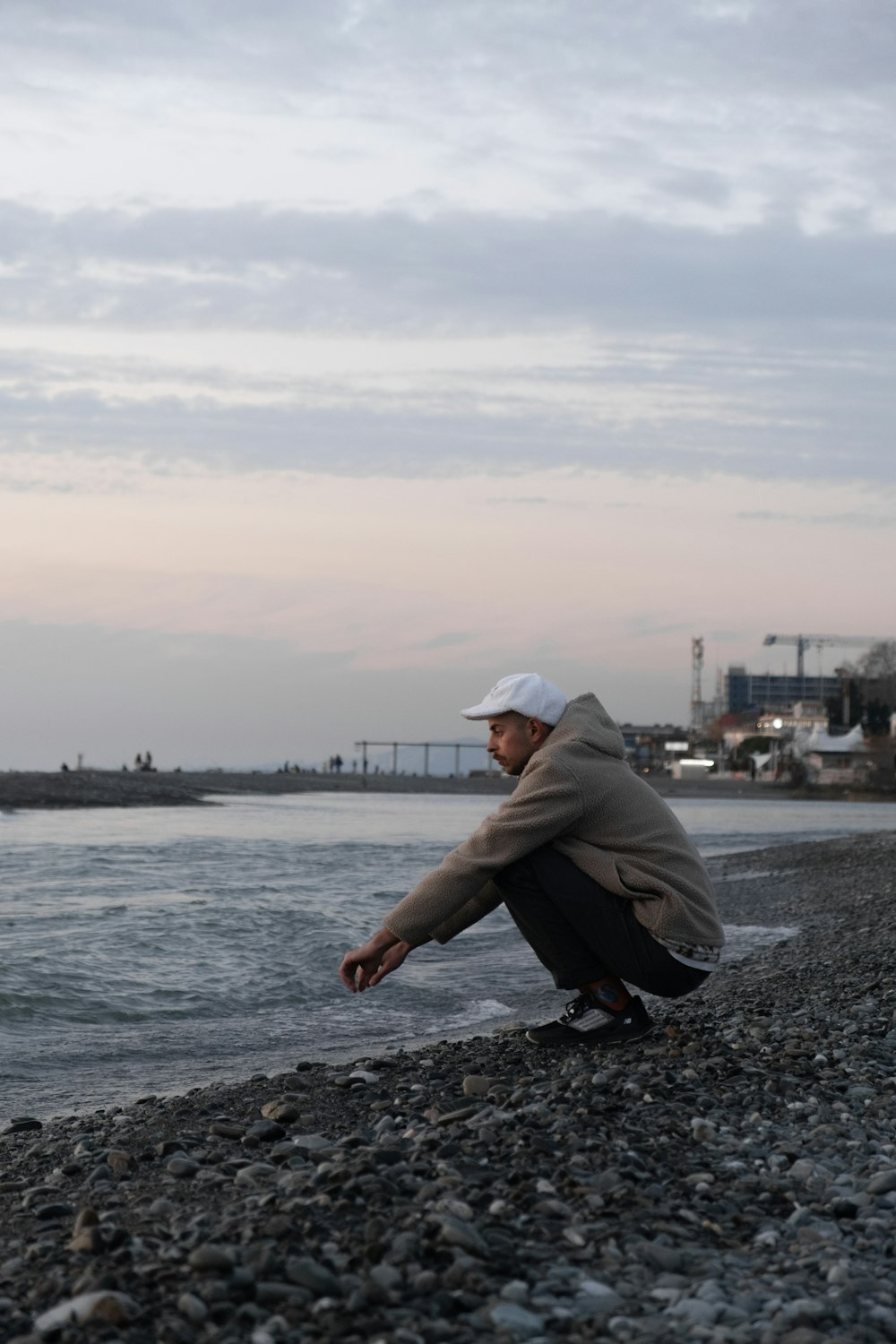 uomo in felpa con cappuccio grigia e pantaloni neri seduto sulla costa rocciosa durante il giorno