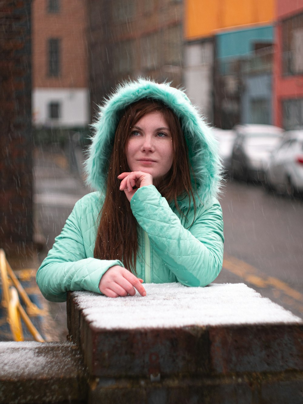 woman in teal hoodie sitting on brown wooden bench during daytime