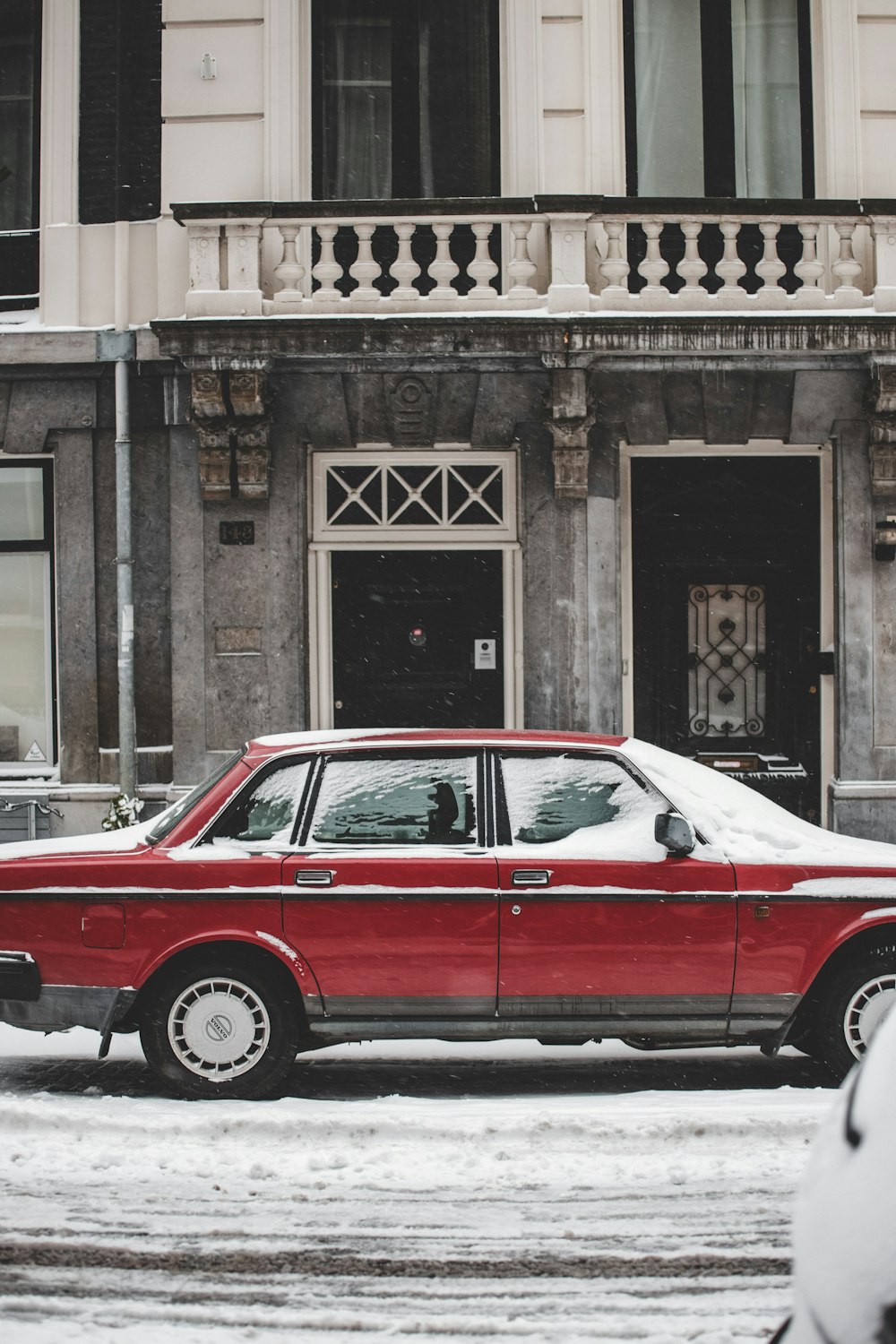 red sedan parked beside brown concrete building during daytime