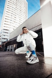 boy in white hoodie and blue pants sitting on gray concrete floor during daytime