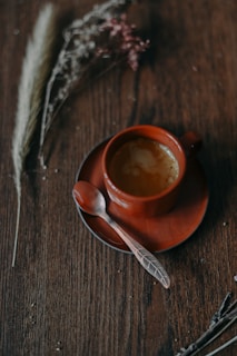 A rustic wooden table with a small bowl of vibrant red chili flakes and a cup of freshly brewed coffee.