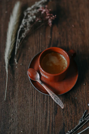 Warm cup of specialty coffee on a wooden table next to a small ceramic pot and vintage spoon