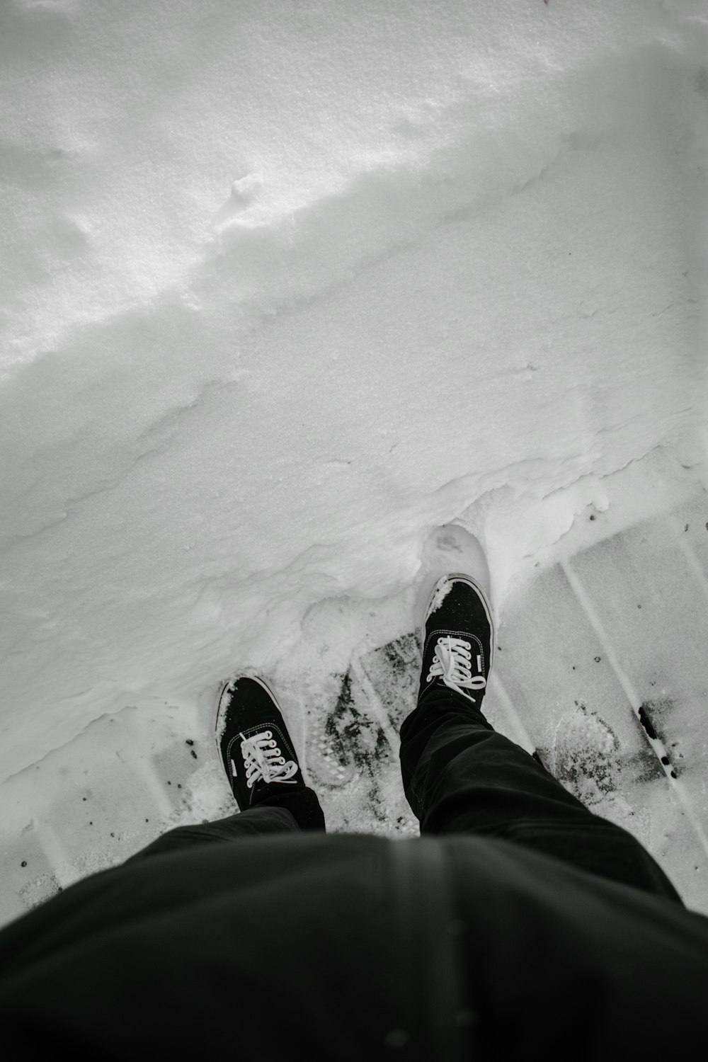person in black pants and black and white sneakers standing on snow covered ground