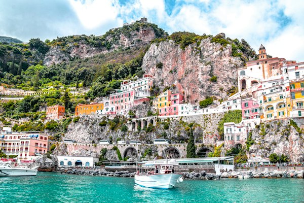 Colorful buildings on a rocky cliffside above the turquoise water in Amalfi, Italy
