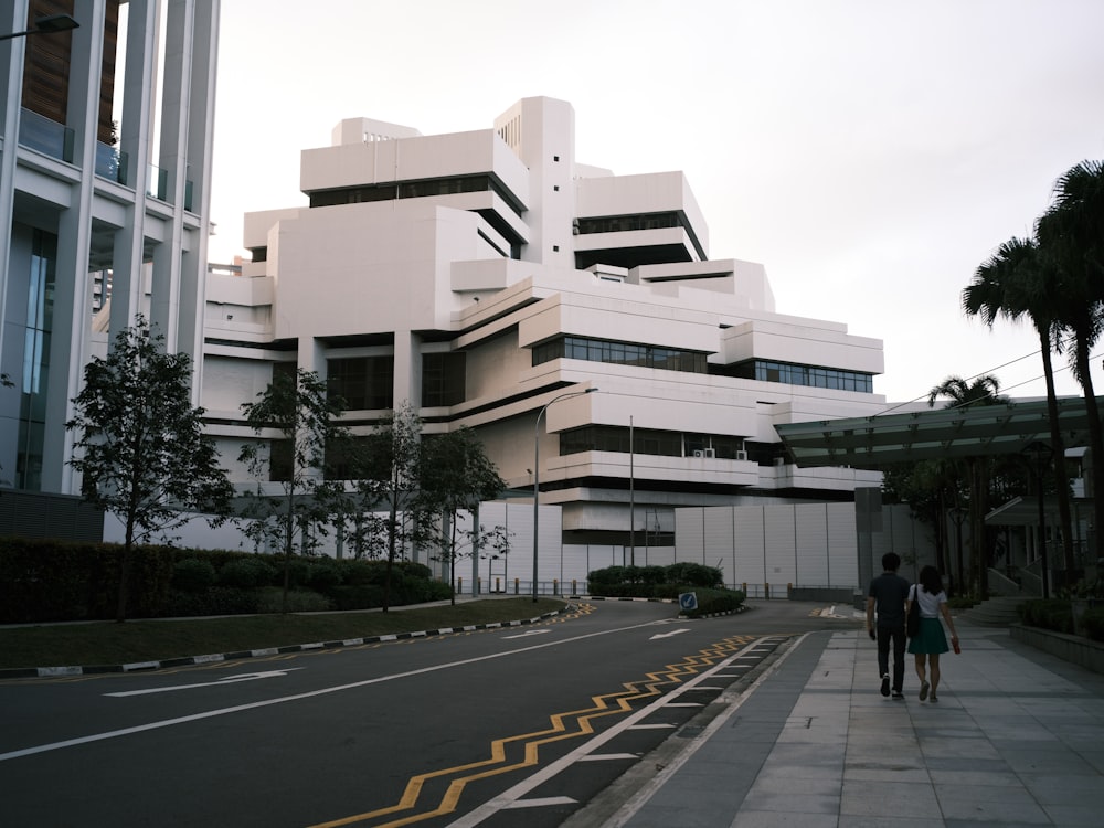 people walking on sidewalk near white concrete building during daytime