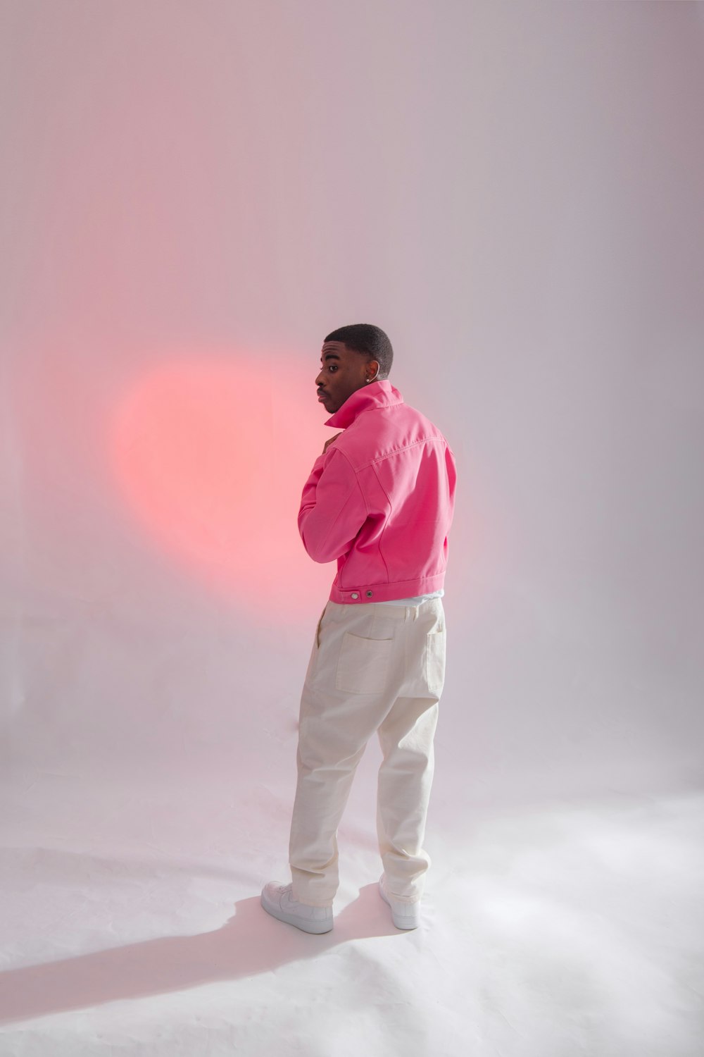man in pink dress shirt and white pants standing