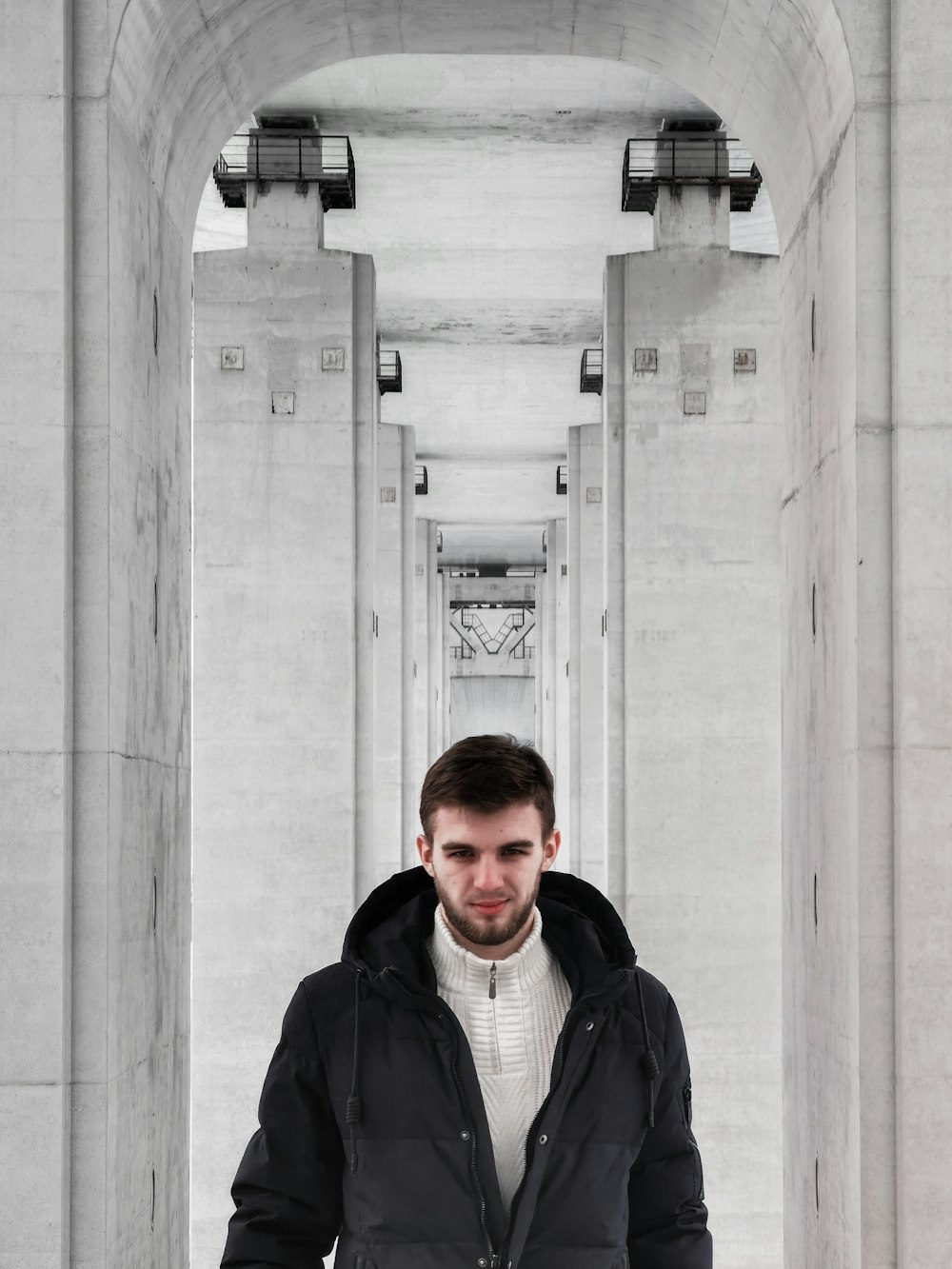 man in black jacket standing near gray concrete wall