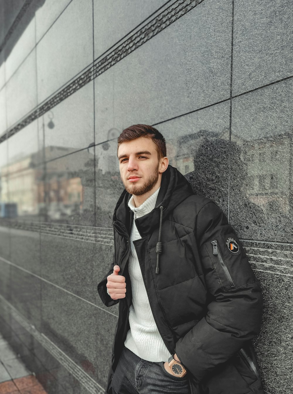 Un uomo appoggiato a un muro che indossa una giacca nera