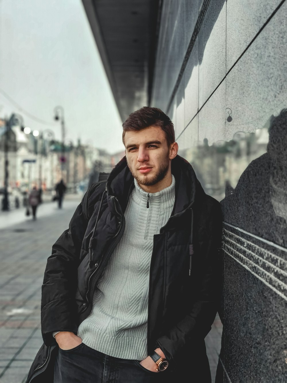 man in black leather jacket standing near gray wall during daytime