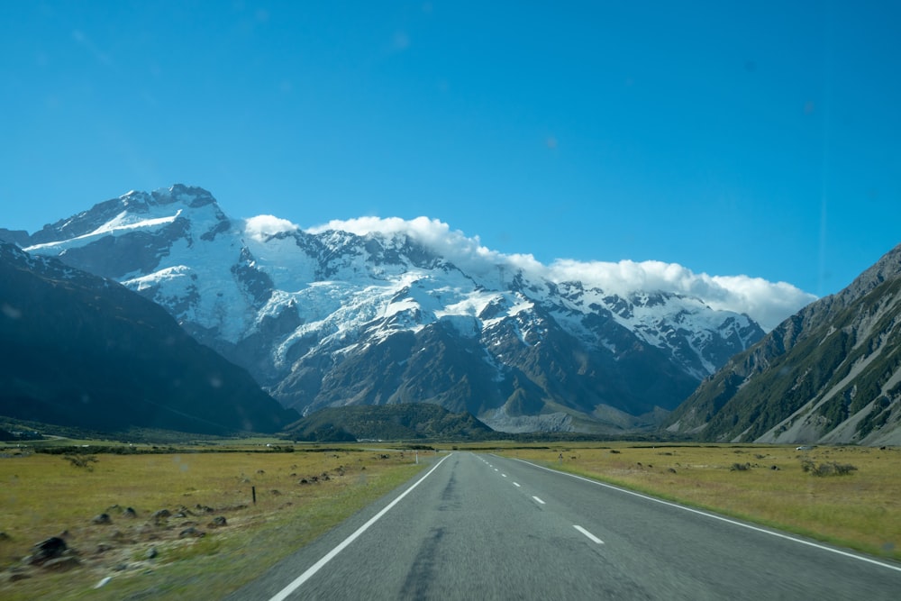 gray concrete road near snow covered mountain under blue sky during daytime