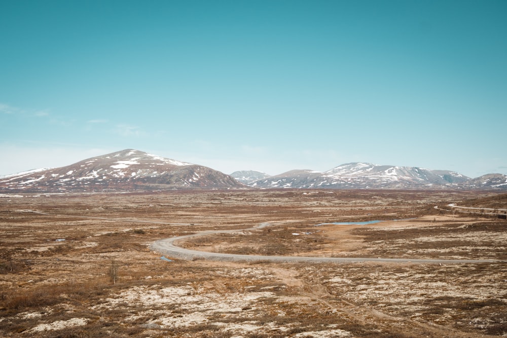 brown field near snow covered mountain under blue sky during daytime