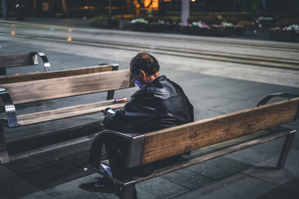 man in black jacket sitting on brown wooden bench