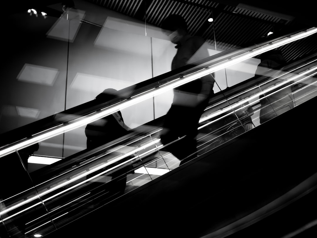 person walking on escalator in grayscale photography