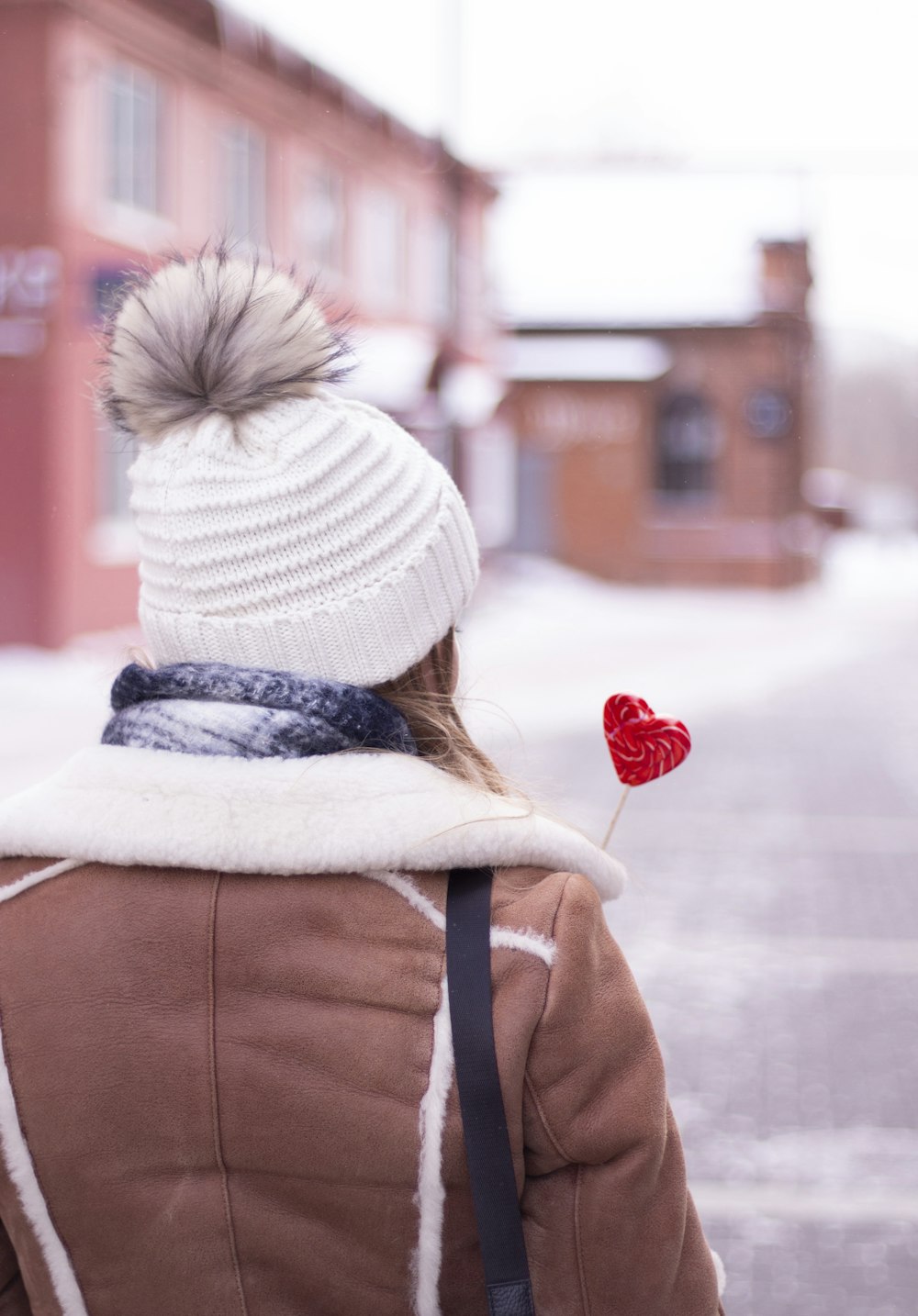 person in brown jacket and white knit cap holding red heart balloon